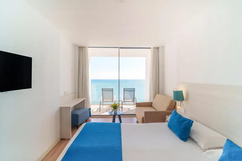 Chambre lumineuse avec canapé et vue sur la mer depuis une baie vitrée.