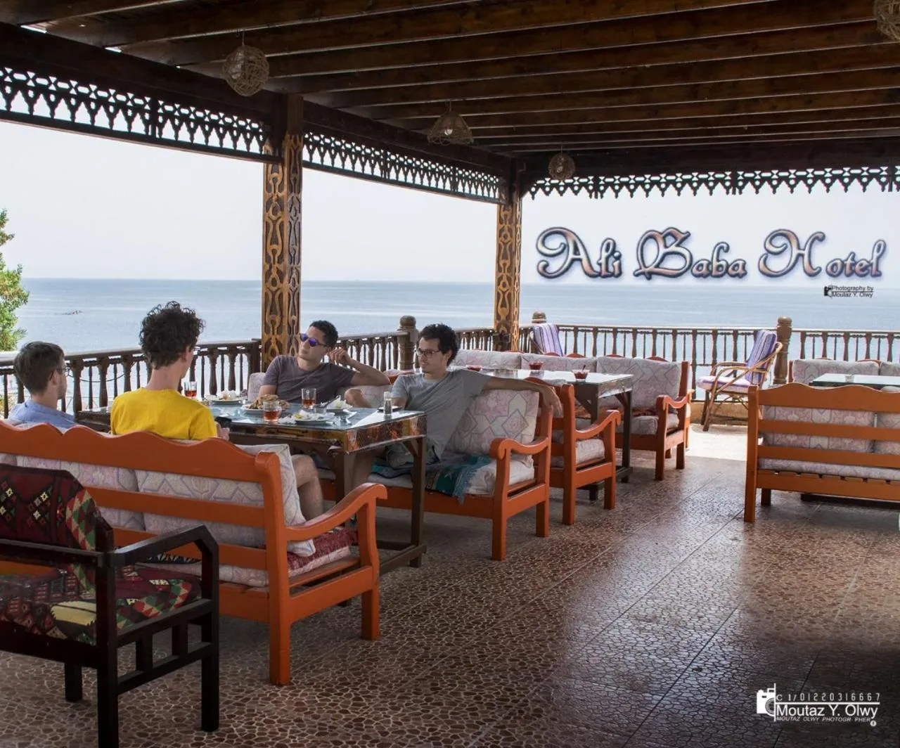 Des clients sont assis à des tables dans un espace extérieur ombragé avec vue sur la mer.