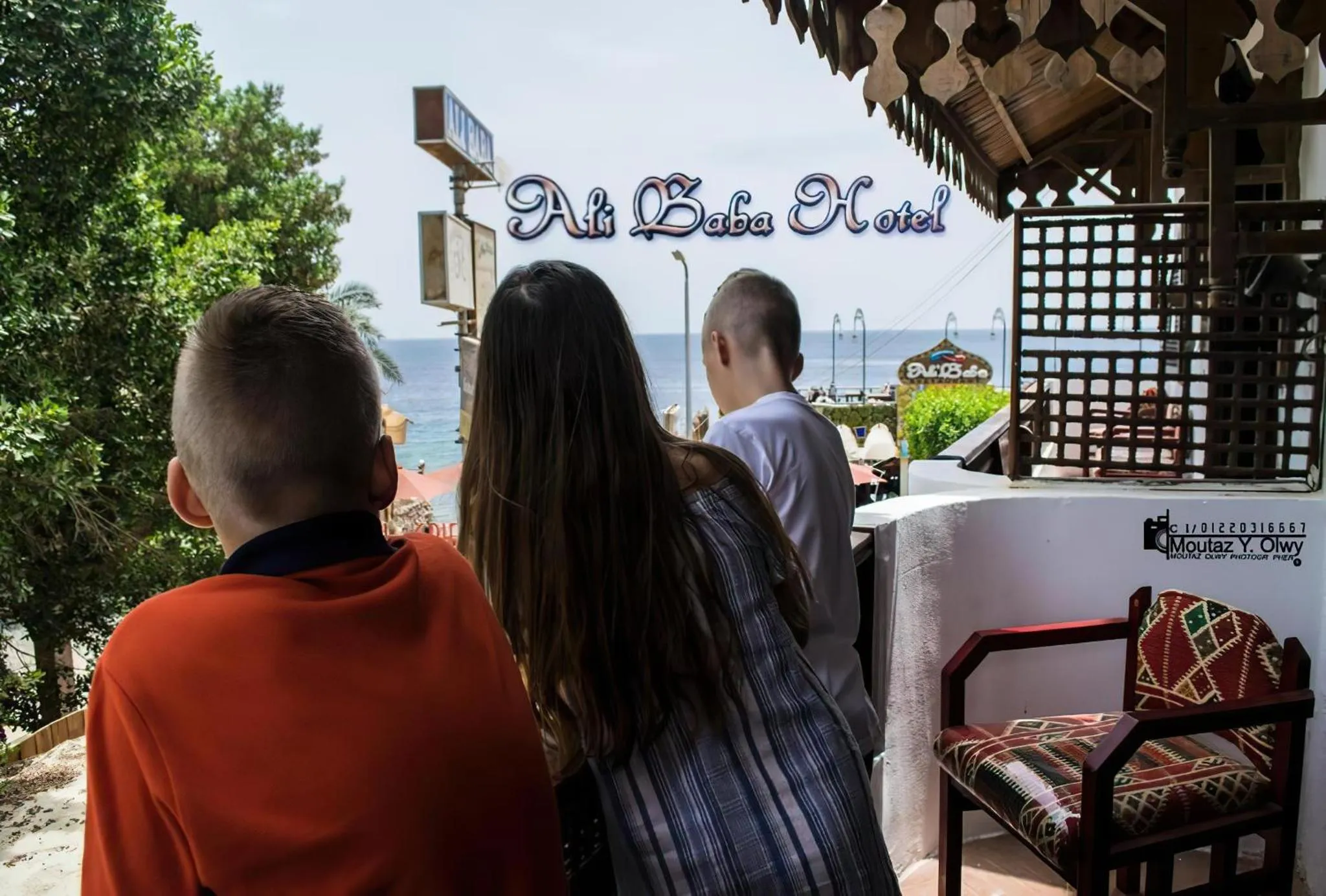 Vue sur la mer depuis une terrasse ombragée avec des personnes au premier plan.