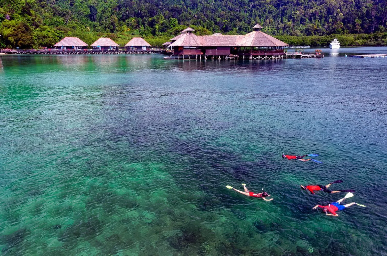 Cabanes sur pilotis au-dessus d'une eau turquoise, avec des nageurs en surface.