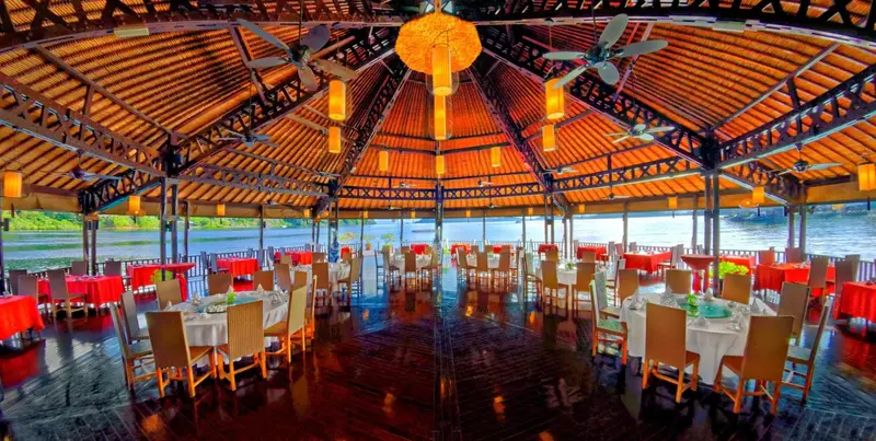 Une salle à manger spacieuse avec des tables dressées et des ventilateurs au plafond.
