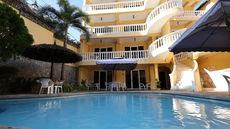Bâtiment jaune à balcons surplombant une piscine et une terrasse ombragée.