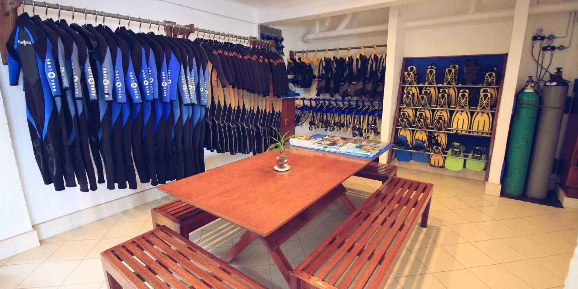 Une salle lumineuse présente des combinaisons de plongée suspendues et du mobilier en bois.