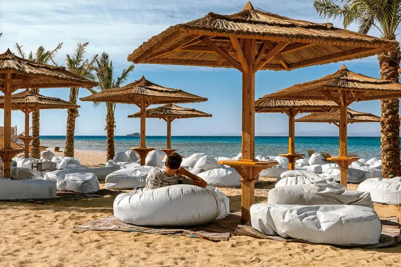 Espace de détente sur une plage de sable avec des parasols en chaume et des fauteuils gonflables.