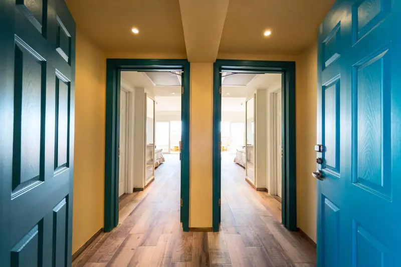 Couloir d'hôtel avec deux portes ouvertes sur des chambres lumineuses.