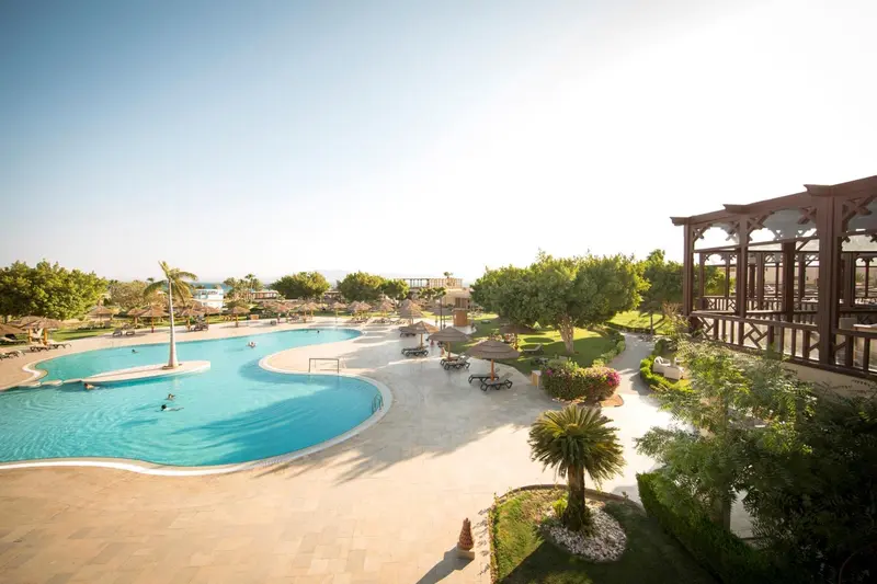 Vue aérienne d'une piscine sinueuse entourée d'un jardin luxuriant et de bâtiments bas.