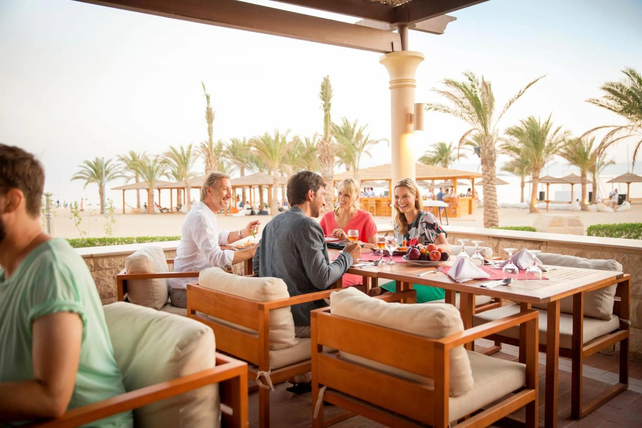 Des convives sont attablés sur une terrasse ensoleillée avec vue sur la mer.