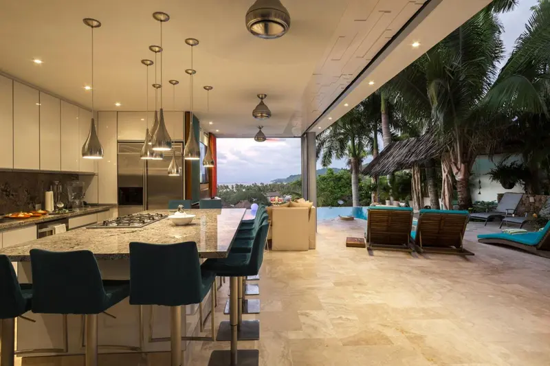 Une cuisine moderne s'ouvre sur une terrasse avec vue sur la végétation et la mer.