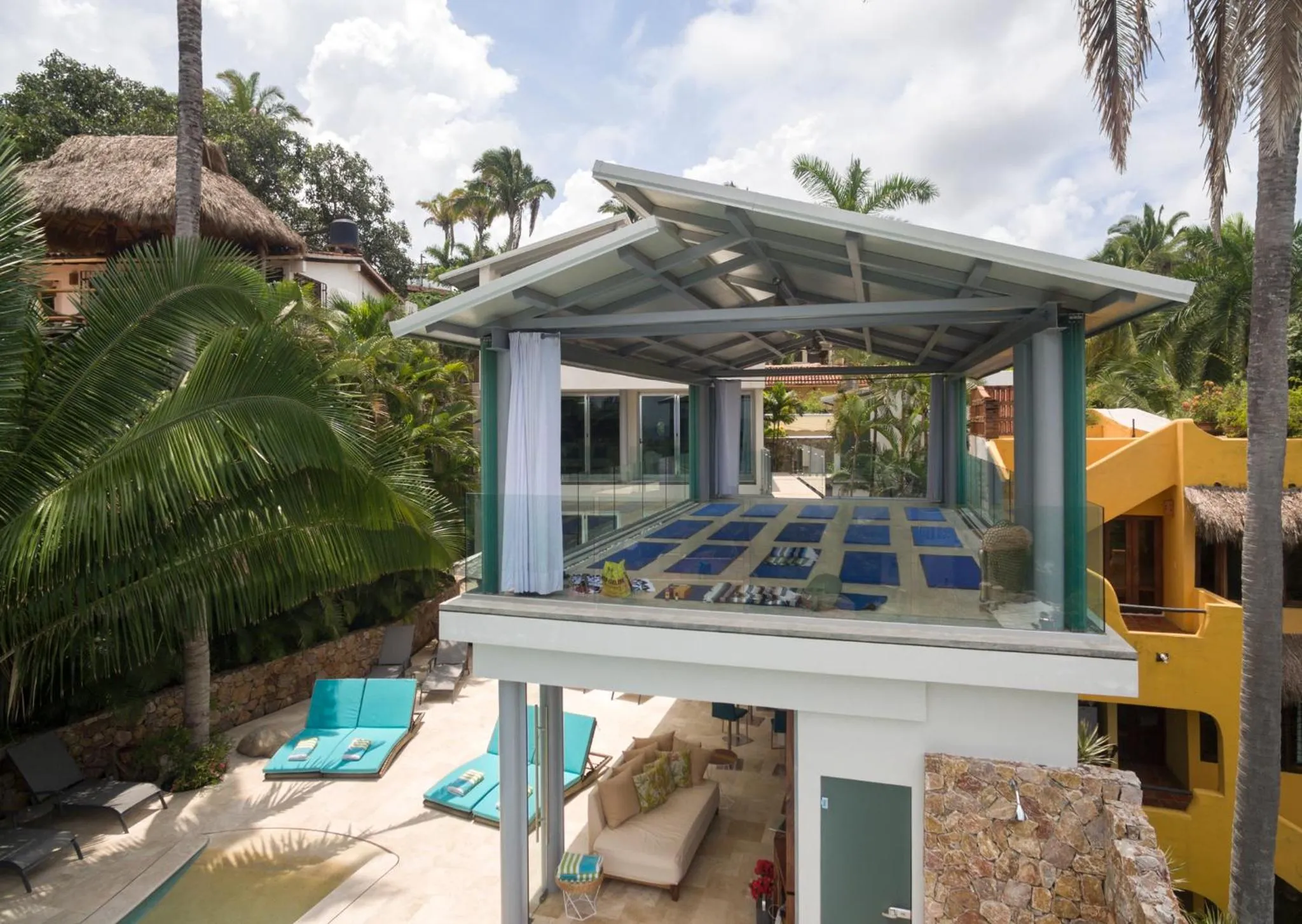 Terrasse ombragée avec salon et chaises longues près d'une piscine.