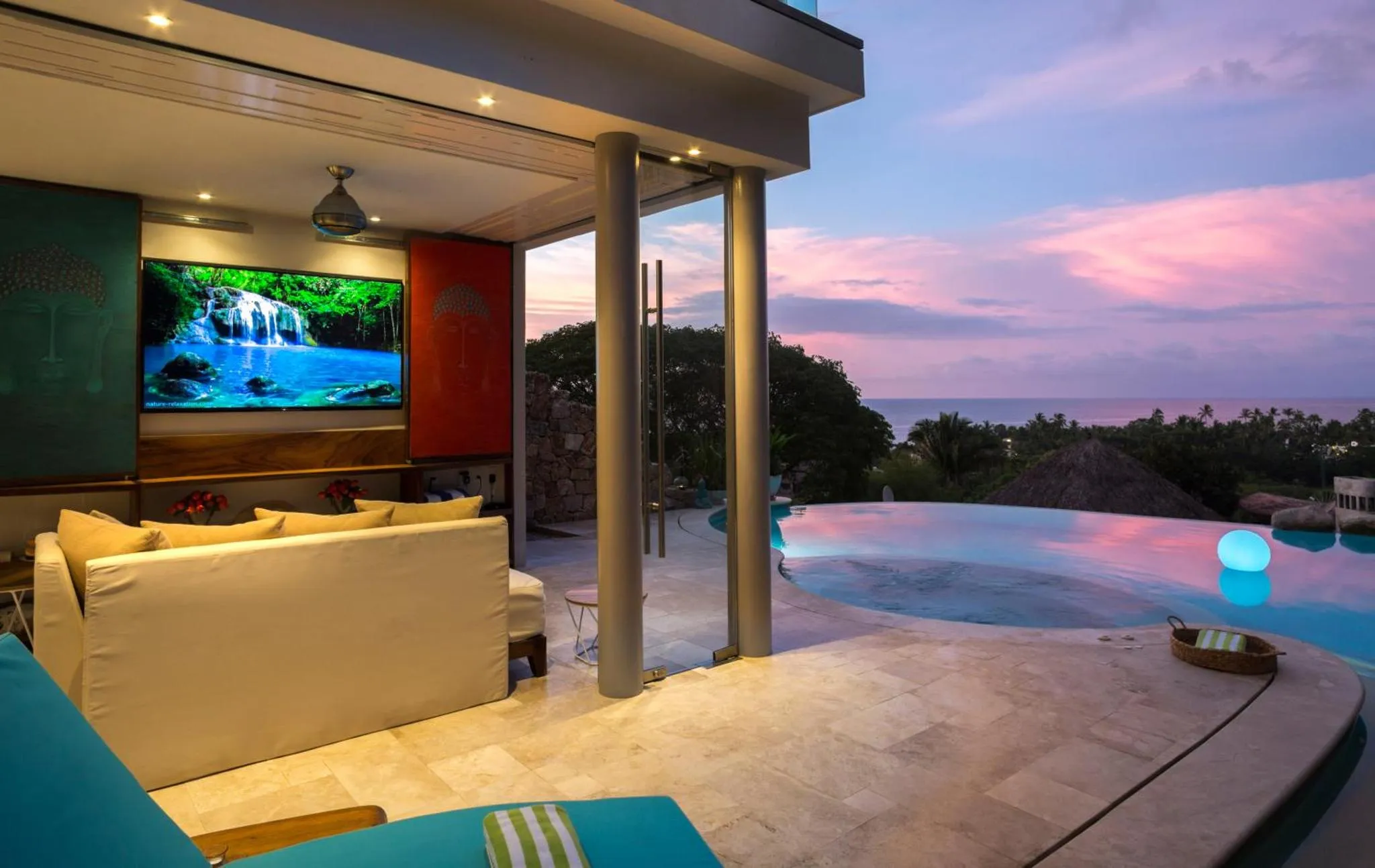 Espace de détente intérieur avec canapés et vue sur une piscine et la mer au crépuscule.