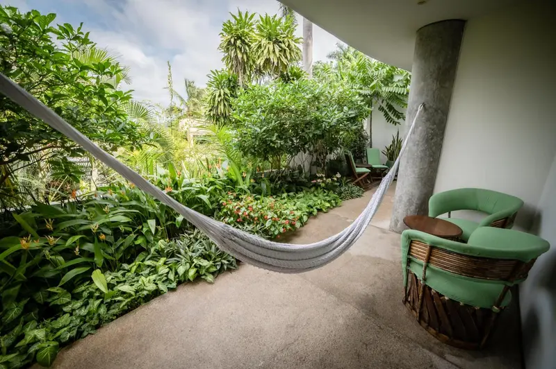 Un hamac blanc est suspendu entre des plantes luxuriantes et des meubles de jardin.