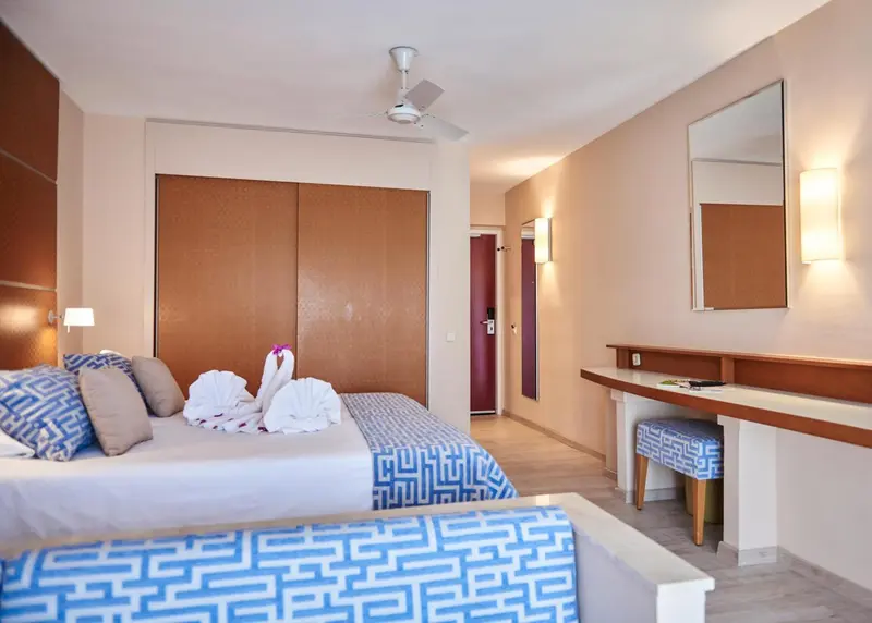 Chambre lumineuse avec un grand lit recouvert d'une couette à motifs et d'oreillers décorés.
