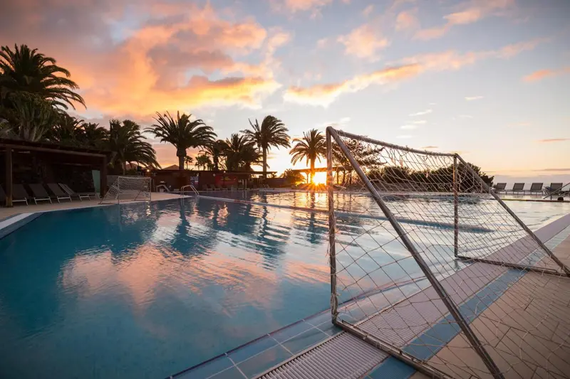 Une piscine avec un filet de volley-ball au premier plan, baignée par les couleurs d'un coucher de soleil.