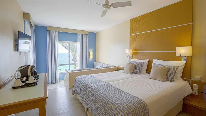 Chambre lumineuse avec un grand lit et vue sur la mer.