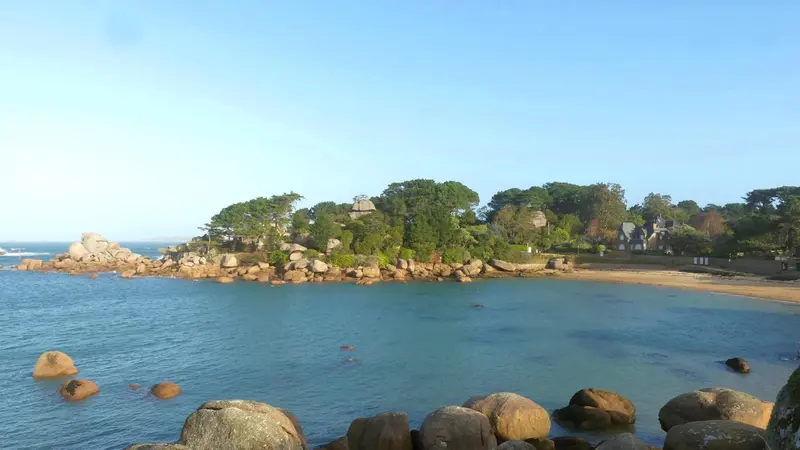 Vue d'une plage de sable fin bordée de rochers et de végétation luxuriante.