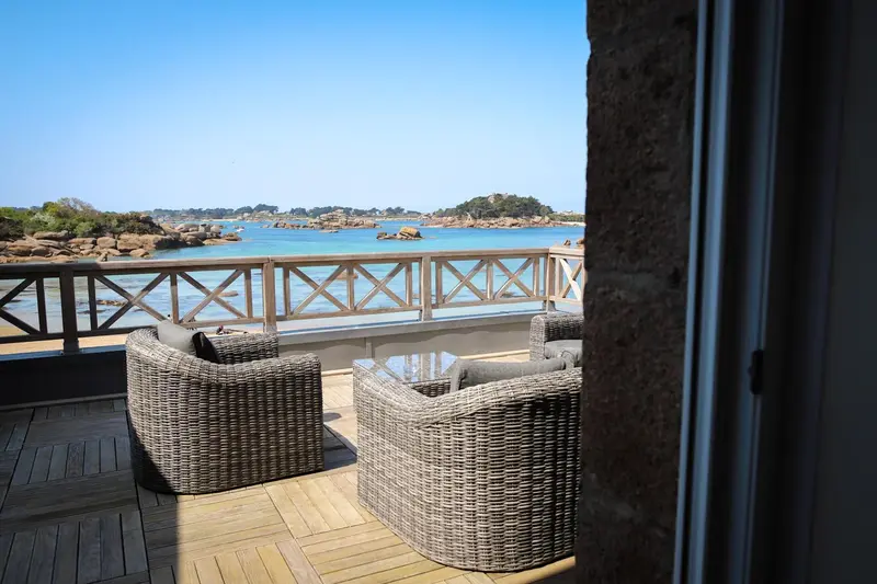 Terrasse aménagée avec mobilier en osier donnant sur une île rocheuse.