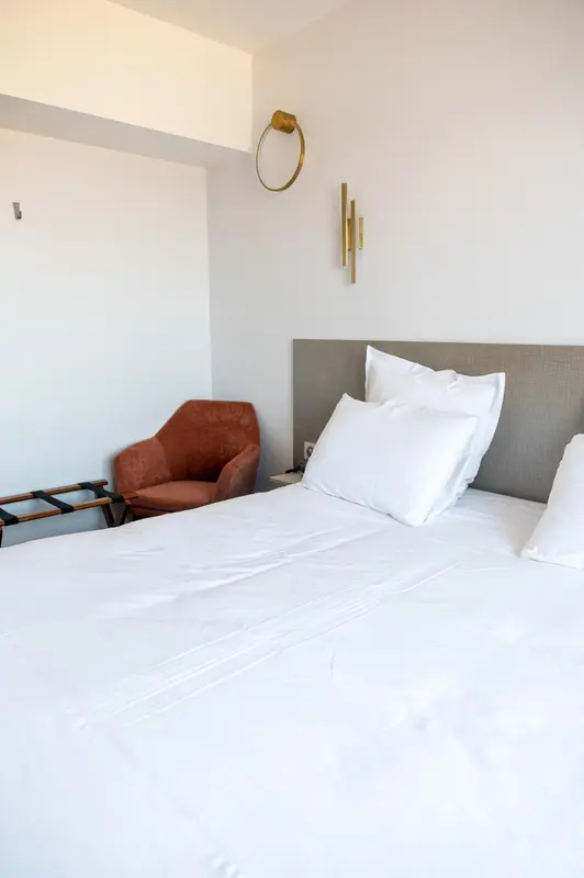 Une chambre lumineuse avec un lit fait et un fauteuil.