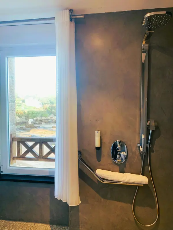 Une douche à l'italienne moderne avec un rideau blanc et une vue sur un paysage côtier.