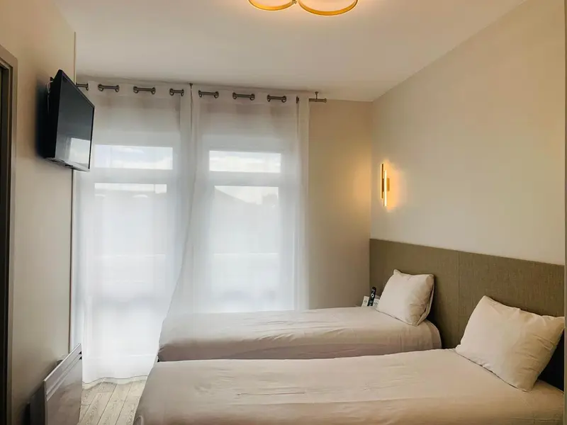 Une chambre lumineuse avec deux lits simples et un téléviseur mural.