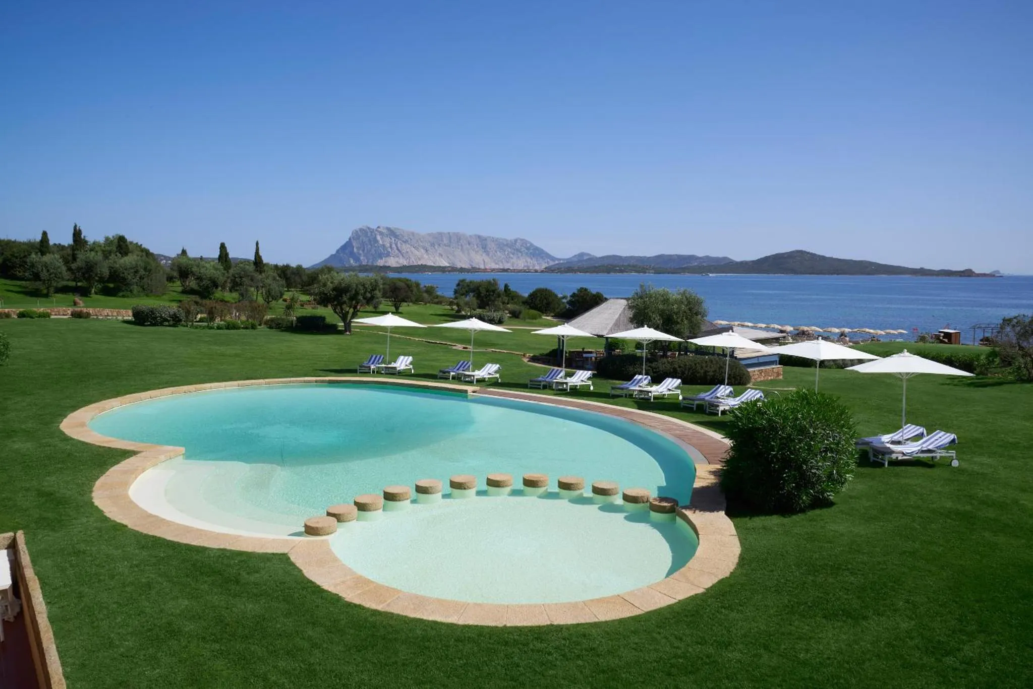 Piscine extérieure avec transats et parasols, vue sur la mer et les montagnes.