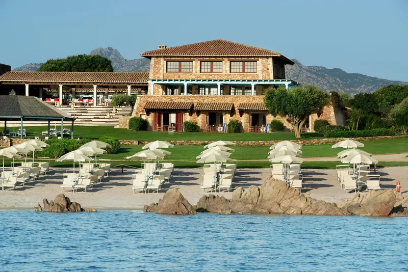 Vue d'un bâtiment bas avec des transats et parasols sur une plage de sable.