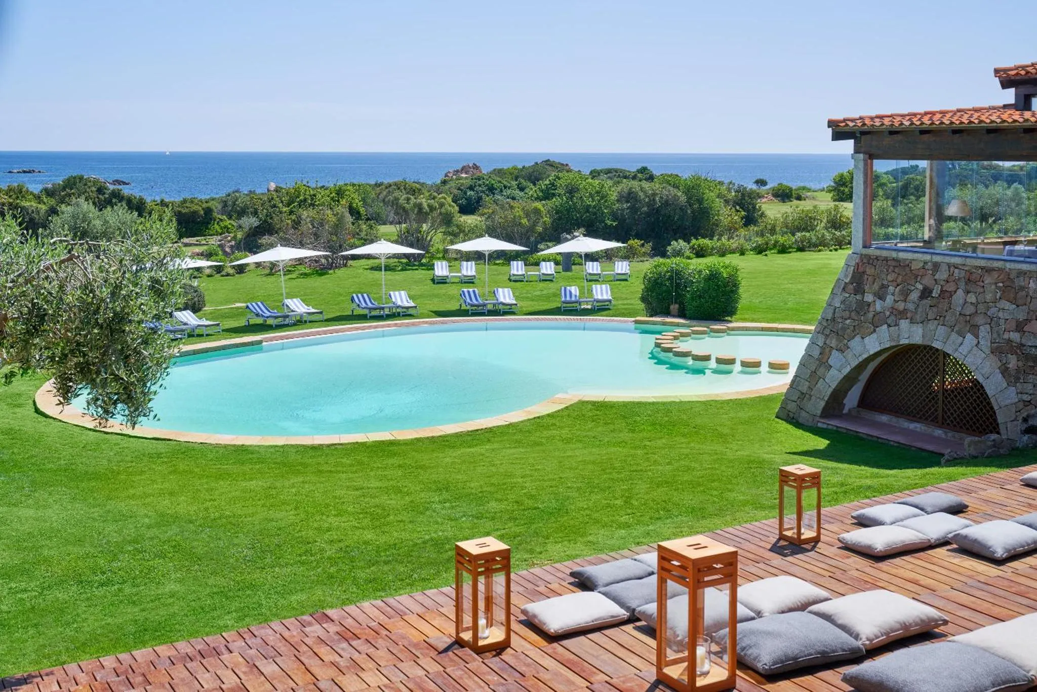 Une piscine bordée de transats et de végétation luxuriante offre une vue sur la mer.