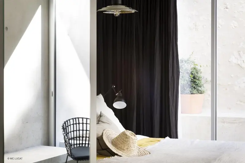Une chambre lumineuse avec un lit recouvert de coussins et une chaise en osier.