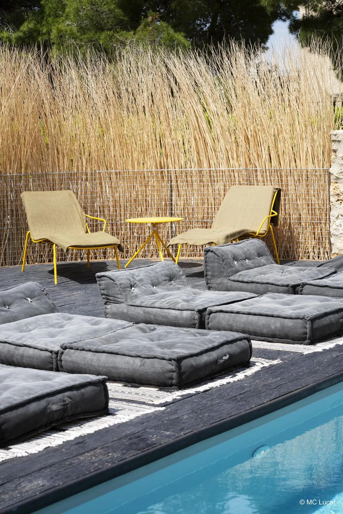 Espace de détente extérieur avec chaises longues et coussins près d'une piscine.