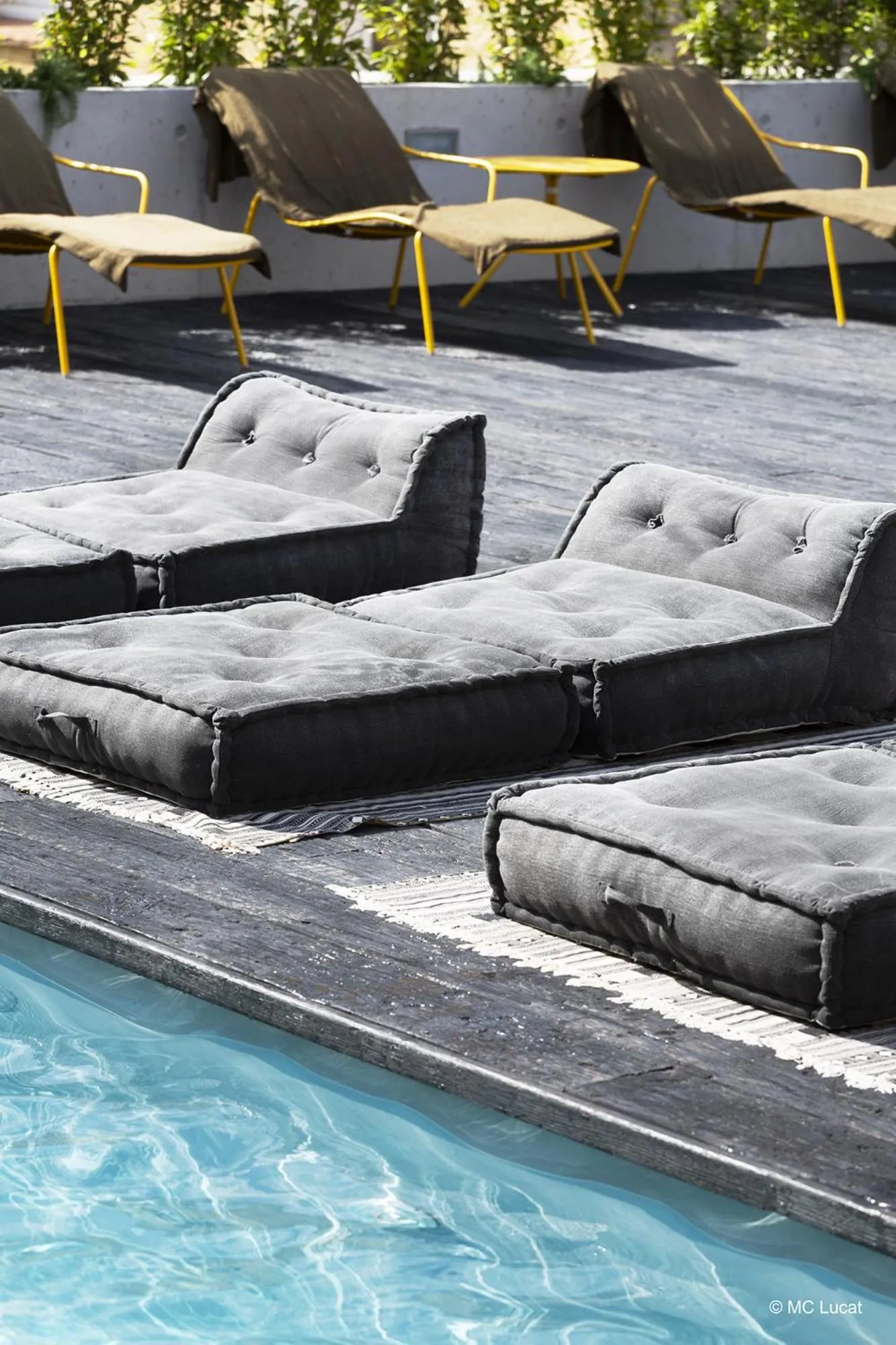 Espace de détente extérieur avec des transats et des coussins près d'une piscine.