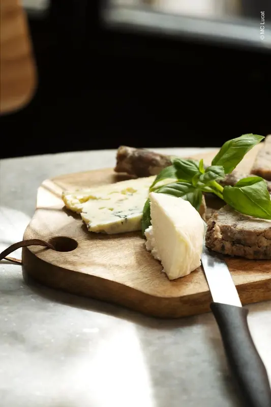Assortiment de fromages sur une planche en bois avec un couteau et des feuilles de basilic.
