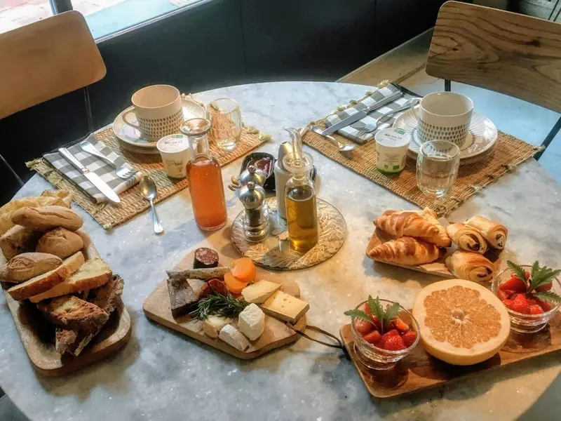 Une table ronde est dressée pour un copieux petit-déjeuner avec des viennoiseries, des fruits et des boissons.