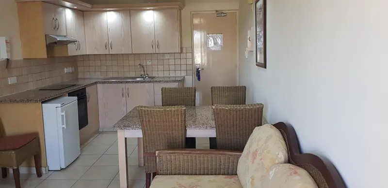 Une cuisine équipée s'ouvre sur un coin repas avec une table et des chaises.