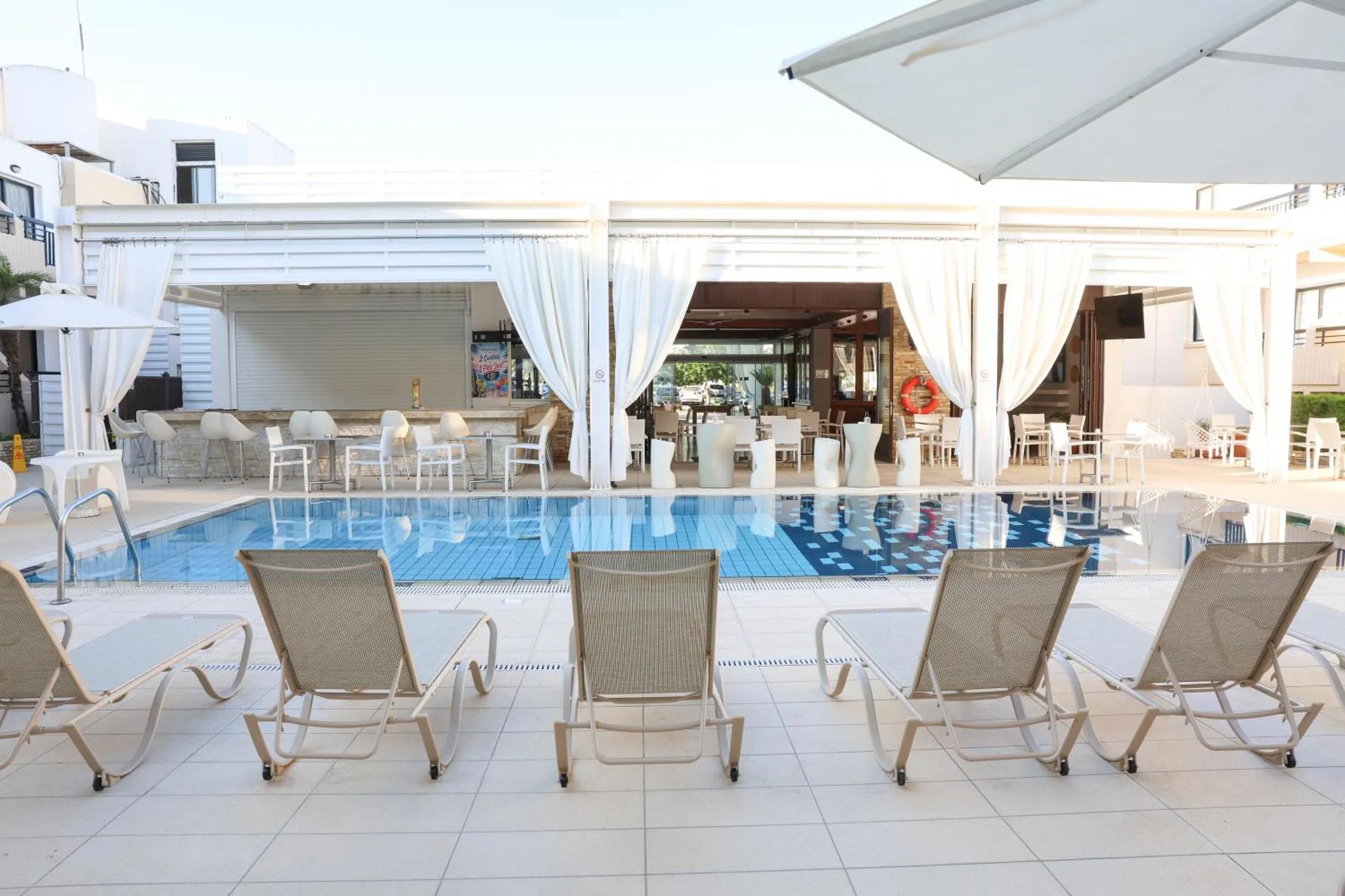 Transats alignés devant une piscine bordée d'un bar et d'une terrasse.