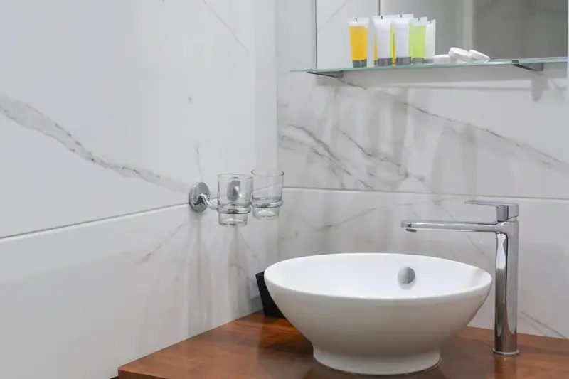 Un lavabo blanc sur un meuble en bois, avec des accessoires de toilette sur une étagère en verre.