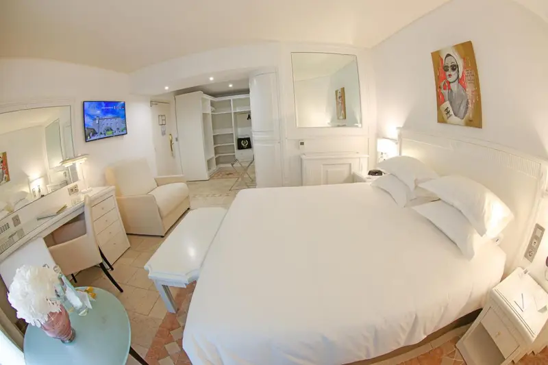 Chambre lumineuse avec un lit blanc et un espace bureau.