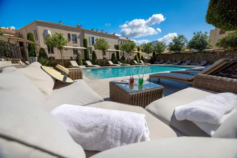 Transats blancs disposés autour d'une piscine bleu turquoise ensoleillée.