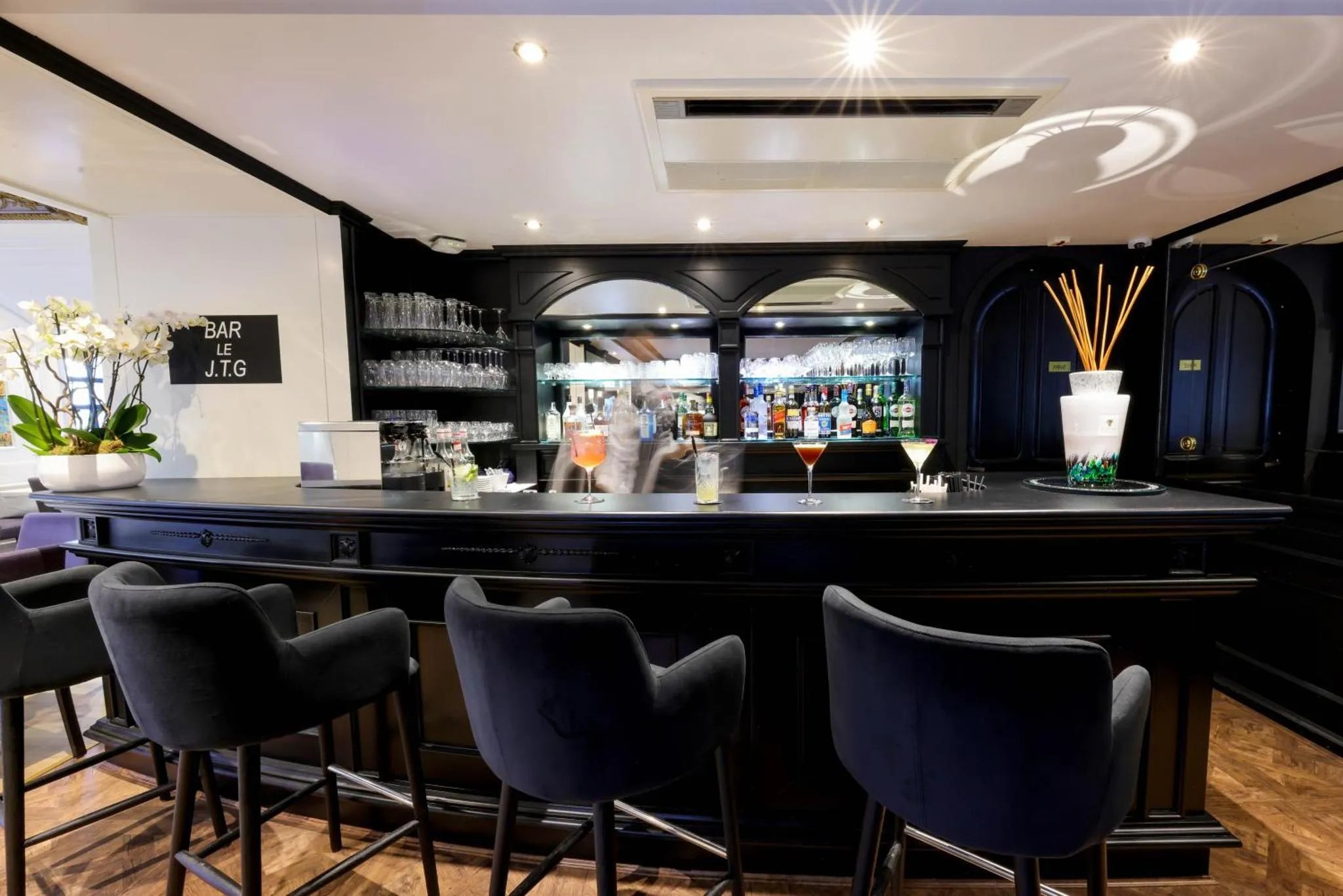 Un comptoir de bar sombre avec des tabourets et des boissons colorées.