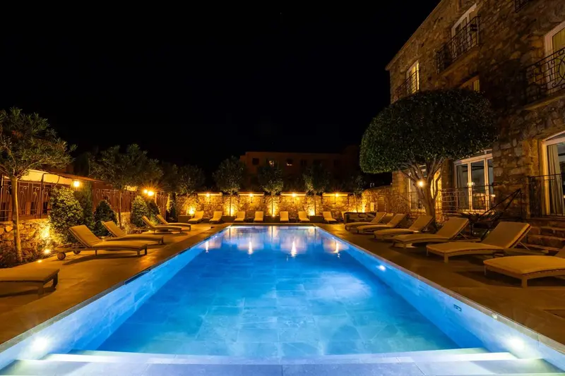 Piscine illuminée avec chaises longues dans un jardin nocturne.