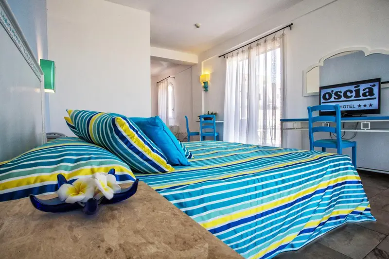 Chambre lumineuse avec un lit recouvert d'un couvre-lit rayé et des coussins colorés.