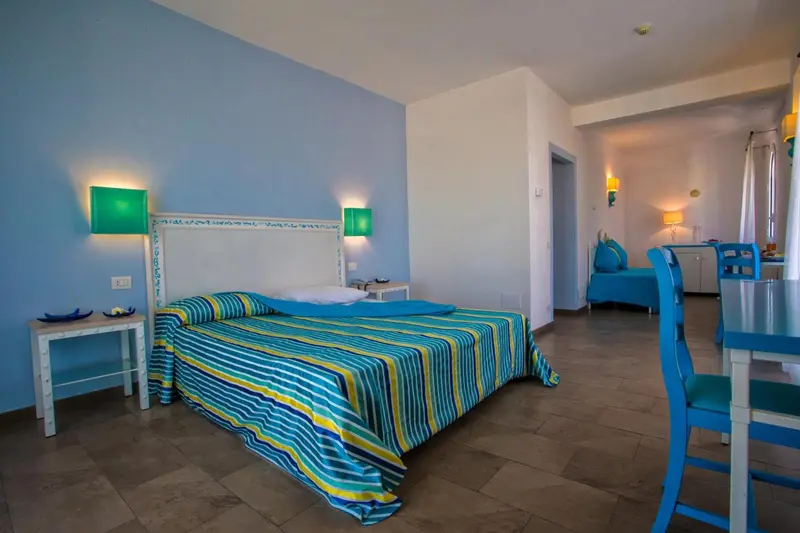 Chambre lumineuse avec un lit recouvert d'un couvre-lit coloré et un coin repas.