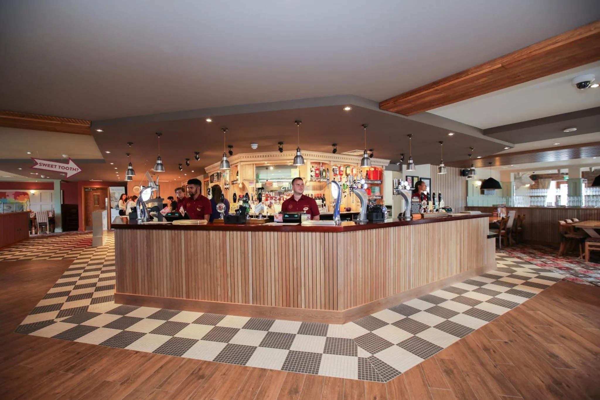 Un bar spacieux avec un comptoir en bois et des clients debout.