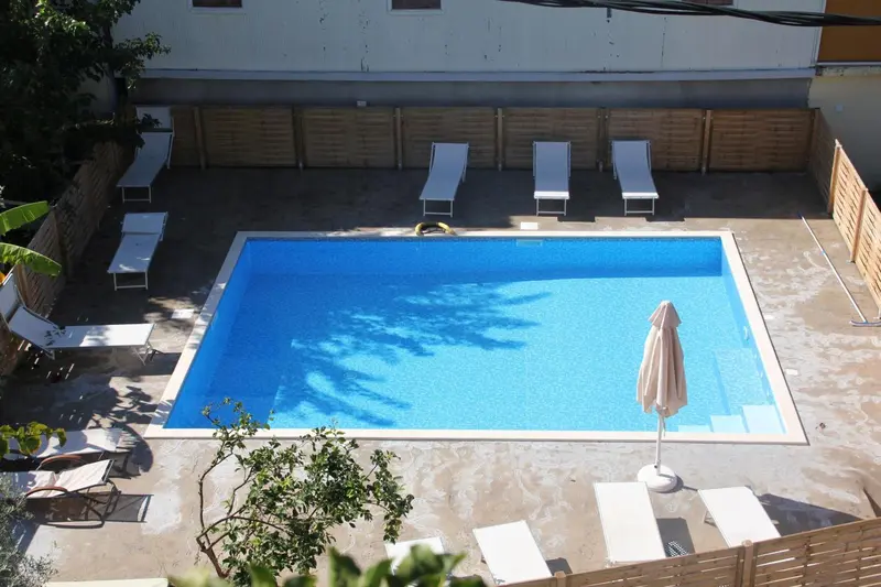 Une piscine rectangulaire entourée d'une terrasse avec des transats et un parasol.