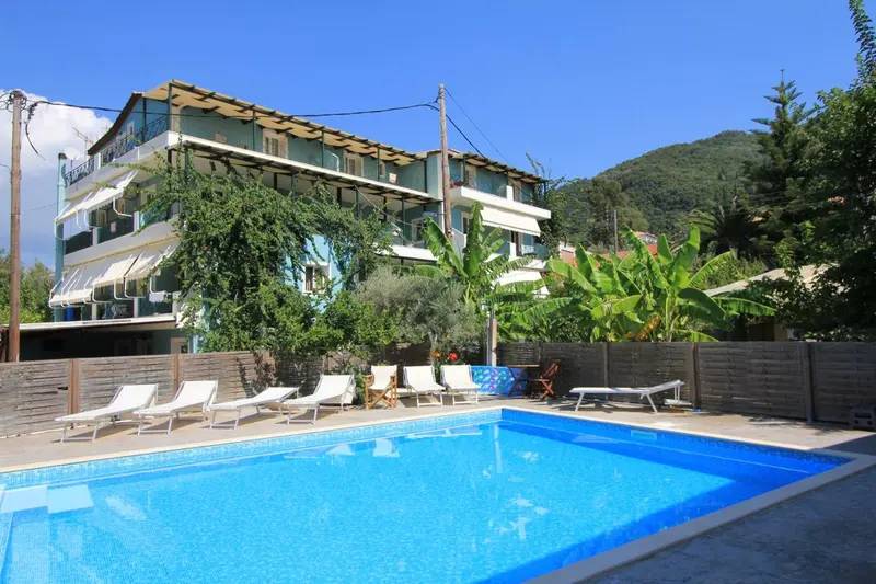 Bâtiment bleu et blanc avec des transats près d'une piscine ensoleillée.