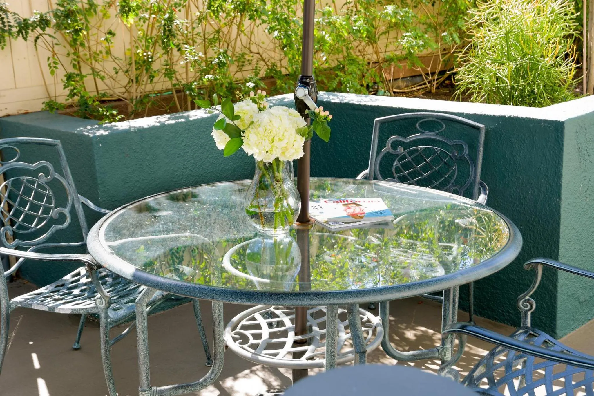 Une table ronde en verre et des chaises en fer forgé sont ornées d'un bouquet de fleurs blanches.
