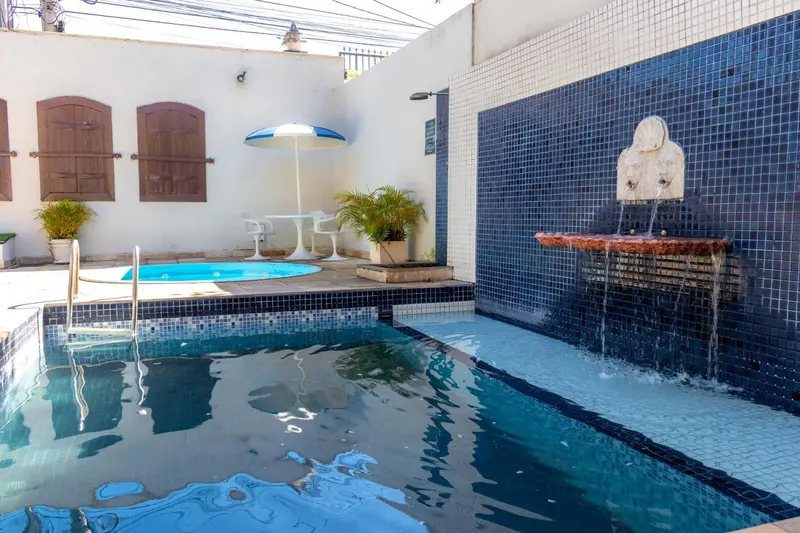 Une petite piscine rectangulaire avec une cascade et des plantes vertes dans une cour carree.