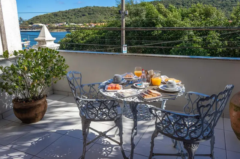 Une table de petit-déjeuner est dressée sur une terrasse ensoleillée avec vue sur la mer.