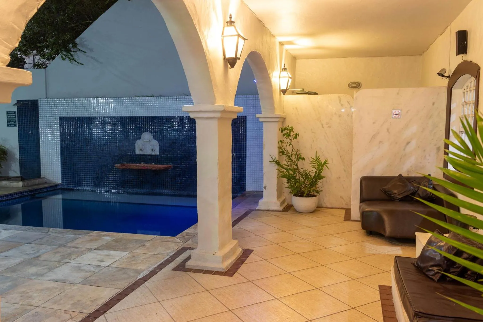 Espace extérieur avec piscine, fontaine murale et mobilier de détente.