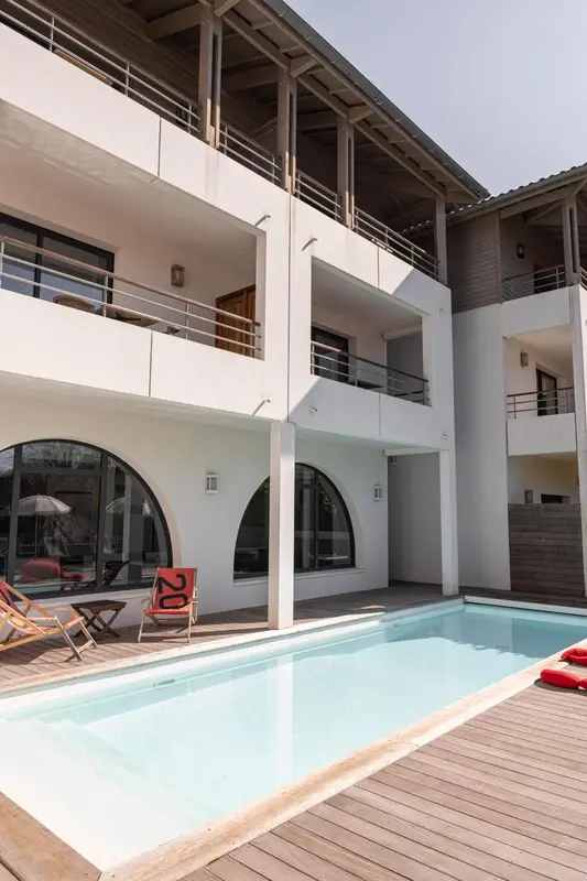 Façade blanche d'un bâtiment avec des balcons et une piscine au premier plan.