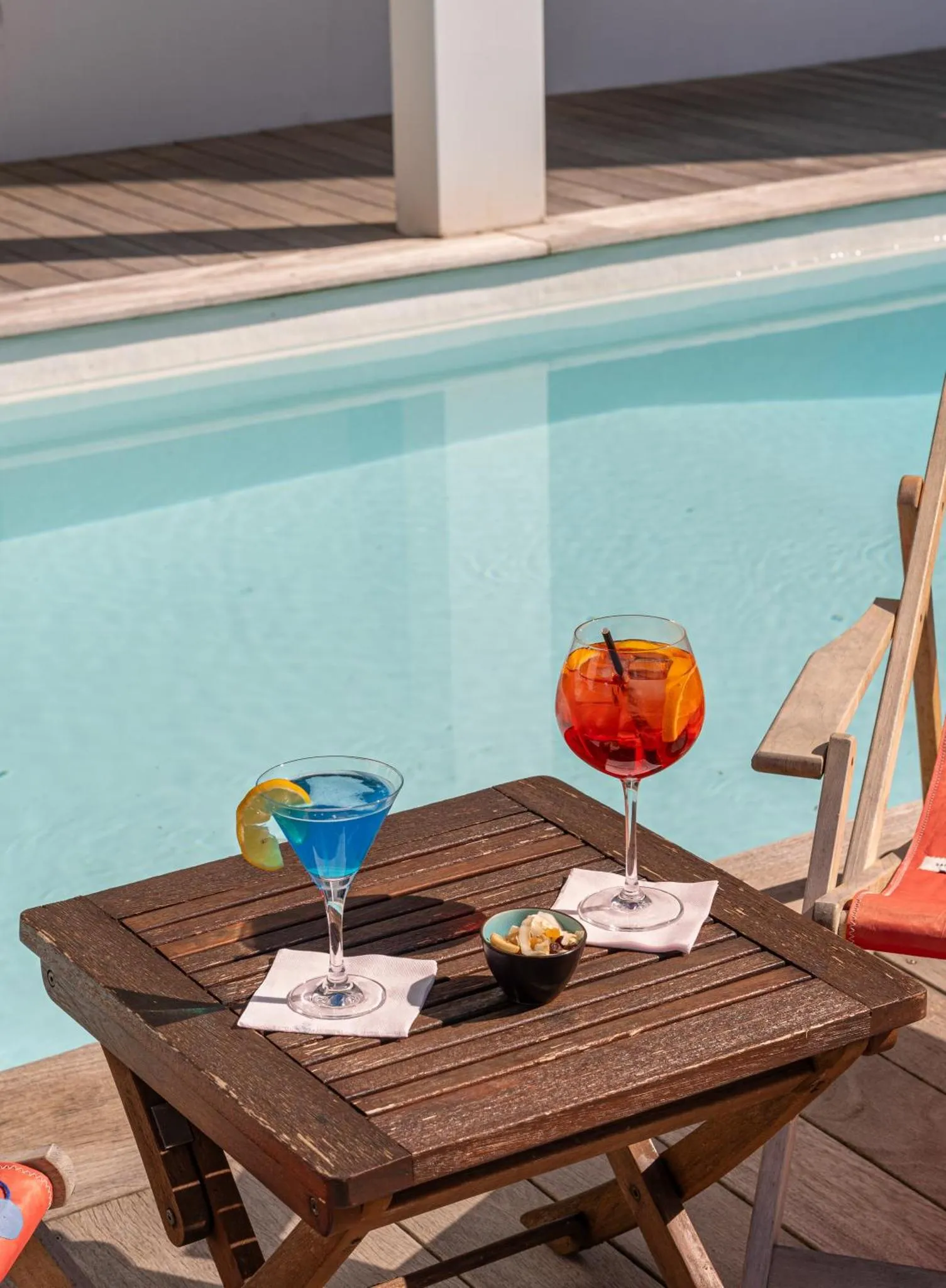Deux cocktails colorés reposent sur une table en bois près d'une piscine.