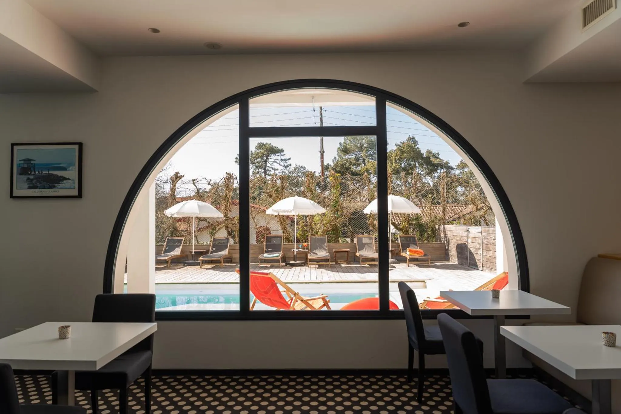 Une salle lumineuse donne sur une piscine et des transats.